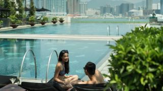 Couple wearing swimsuits on outdoor swimming pool deck, city skyline in background